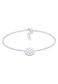 Silverarmband med kedjedesign, prydd med en rund berlock graverad med riktningens bokstäver (N, S, Ö, V) och pilar. Inkluderar en stjärnaccent.