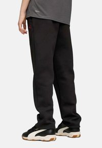 Zwarte joggingsbroek gemaakt van zachte stof, met een ontspannen pasvorm, elastische tailleband en subtiele rode branding. Gecombineerd met zwart-witte sneakers.