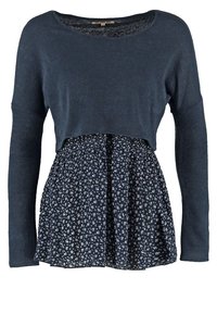 Mörkblå långärmad topp med en kortad design; tyget är mjukt. Nederdelen har ett blommönster på en kontrasterande mörkblå kjol.