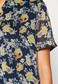 Blusa floral com fundo azul-marinho, adornada com flores amarelas, laranjas e roxas. Mangas curtas, tecido leve e um padrão texturizado.