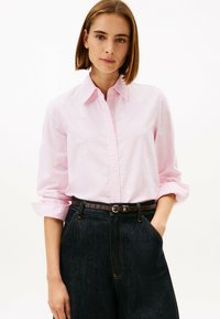 Light pink striped button-up shirt with white floral embroidery, rolled sleeves, and a black belt worn over dark denim jeans.