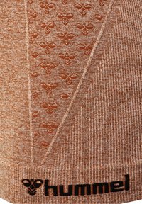 Hnědá látka s vzorem, kterou zdobí jemný design a žebrovaná textura. Podél dolního okraje je černé logo "hummel".