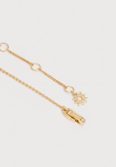 Δύο λεπτές χρυσές αλυσίδες με μικρούς κυκλικούς κρίκους, η μία καταλήγει σε ένα μενταγιόν σχήματος ήλιου και η άλλη σε μια μικρή ορθογώνια αγκράφα.