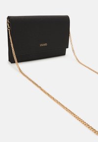 Borsa a mano sintetica nera con superficie texturizzata, chiusura a pattina, tracolla in oro e dettaglio del logo sulla parte anteriore.