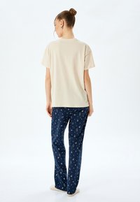 Cremfarbener T-Shirt mit kurzen Ärmeln, kombiniert mit navyblauen Schlafanzughosen, die ein geometrisches Muster, eine glatte Textur und eine lässige Passform aufweisen.