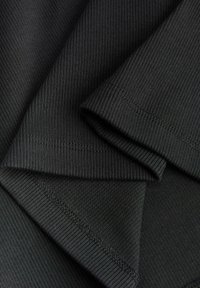 Gros plan d’un tissu noir côtelé plié avec des coutures et des détails de surpiqûres visibles.