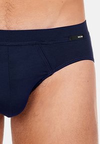 Marineblaue Slips aus glattem Stoff mit enganliegendem Design. Verfügt über ein schwarzes Logo-Detail am Bund. Nahtlose Verarbeitung ist sichtbar.