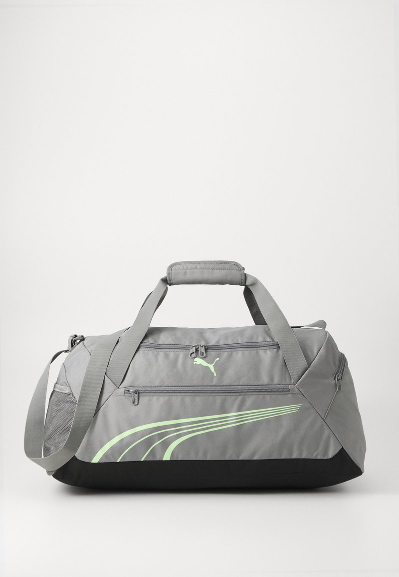 Šedá sportovní taška s černým dnem, vybavená dvojitými zipy, nastavitelným popruhem a logem Puma. Zelené akcentové linky dodávají designu detail.