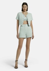 Mintgroen tweed two-delig set met een cropped jasje met knopen, bijpassende strakke shorts en zwarte sandaaltjes met banden.