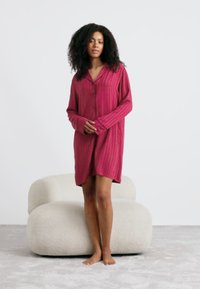 Camicia da notte a maniche lunghe in rosa intenso con motivo a righe e chiusura a bottoni. Tessuto morbido e fluido con vestibilità rilassata. Modello in piedi.
