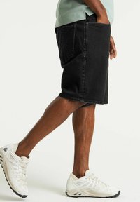 Pantalones cortos de mezclilla negra con un corte recto, dobladillo deshilachado y dos bolsillos laterales. Llevados con zapatillas deportivas blancas con un diseño texturizado.