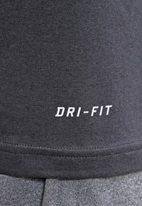 Szara koszulka sportowa Dri-Fit z gładkiego, oddychającego materiału, z wyraźnym białym logo "DRI-FIT" na dolnej części.