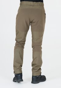 Pantalons de randonnée beiges avec genoux renforcés, ourlets ajustables et une taille élastique, associés à des chaussures de randonnée noires.