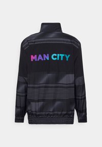 Black jacket with a high collar, featuring the text "MAN CITY" in gradient colors. Textured stripes across the fabric and elastic cuffs.