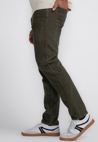 Olijfgroene corduroy broek met een rechte pasvorm. Voorzien van zij- en achterzakken, gecombineerd met witte sneakers met zwarte accenten en een gumrubberen zool.