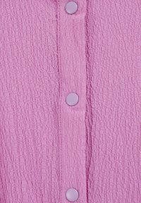 Texturovaná růžová látka s zvrásněným povrchem, s světlými fialovými knoflíky podél vertikální lišty.