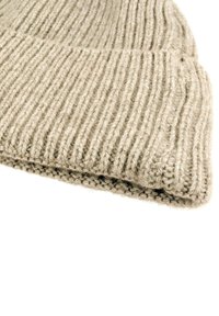 Beige knit beanie featuring a ribbed texture, fold-over brim, and subtle variation in yarn thickness, made from soft wool blend material.