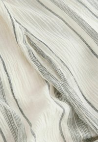 Tissu blanc avec des rayures verticales noires, comportant un détail plissé créant des plis texturés et des lignes superposées.