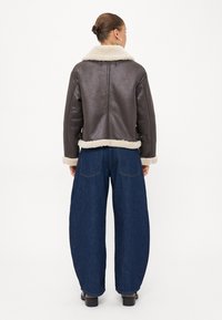 Giacca di pelle marrone con collo e polsini in shearling crema, abbinata a jeans in denim blu scuro a gamba larga e vita alta.