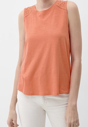 Top coral sin mangas con detalles de encaje con ojales en los hombros, llevado con pantalones de color claro en una persona frente a un fondo liso.
