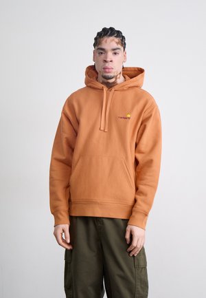 Orange hooded sweatshirt with a front pocket, featuring a small embroidered logo. Paired with olive green cargo pants.
