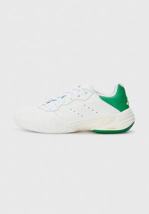 Hvid atletiksneaker med grøn hæl, snøredesign, perforerede sidedetaljer og tekstureret sål på ensartet lys baggrund.