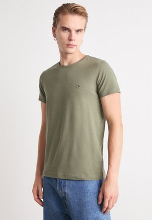 Maglietta verde oliva a maniche corte in cotone con scollo rotondo, dotata di un piccolo logo sul petto. Tessuto liscio, vestibilità regolare.