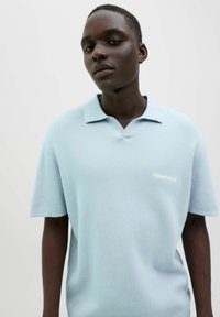 Lys blå kortærmet polo shirt med struktureret væv, standard krave og en diskret mærkebroderi på venstre bryst.