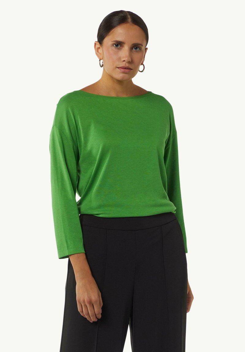 Groen longsleeve top met een wijde bootnek, gemaakt van een gladde stof, gecombineerd met hoge zwarte broek.