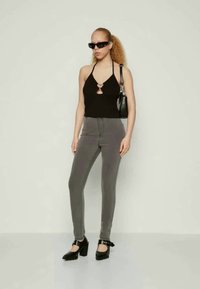 Μαύρο τοπ με λαιμόκοψη, γκρι παντελόνι με ψηλή μέση και χοντρές μαύρες γόβες. Τα αξεσουάρ περιλαμβάνουν μικρή μαύρη τσάντα και γυαλιά ηλίου.