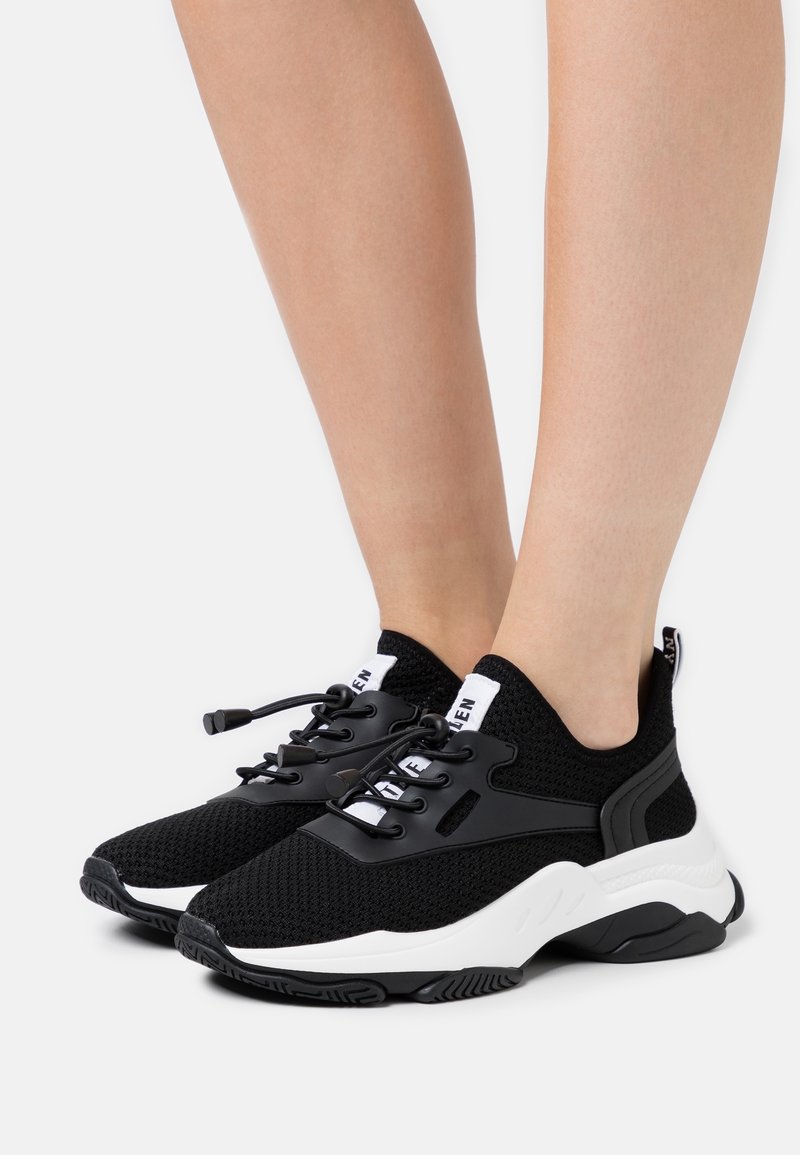 Schwarze Strick-Sneaker mit weißen Akzenten, Gummisohle, strukturierter Oberseite, elastischen Schnürsenkeln und gepolstertem Kragen für Komfort.