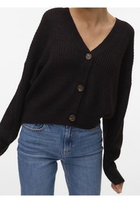 Kardigan z dzianiny w ciemnym brązie, z długim rękawem i dekoltem w serek, z dużymi brązowymi guzikami i luźnym krojem, zestawiony z niebieskimi dżinsami.