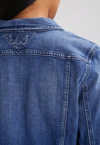 Jeansjacka i mörkblått med en klassisk krage, synlig sömnad och en okdetalj på baksidan för ökad struktur.