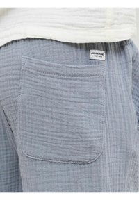 Gros plan d'une poche de pantalon en tissu gris clair texturé avec une petite étiquette de la marque Jack & Jones près de la ceinture.