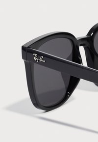 Ochelari de soare Ray-Ban negri cu un design geometric îndrăzneț. Prezintă lentile întunecate și un logo lucios pe brățară. Cadru din plastic neted.