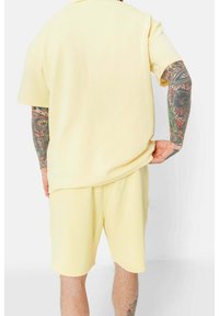 Conjunto de camiseta y pantalones cortos a juego en color amarillo, hecho de una tela suave. Presenta un corte relajado y mangas cortas, con una textura suave y un diseño minimalista.