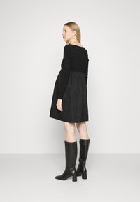 Vestido preto com corpete canelado e saia ampla. Acompanhado de botas de couro pretas até o joelho e brincos. Design simples, cor sólida.