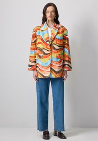 Multicolored blazer with wavy patterns in orange, blue, and yellow. Features large lapels and two buttons. Paired with straight-leg denim jeans.
