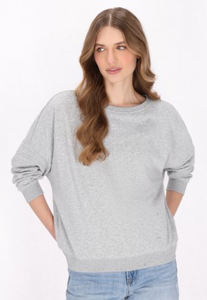 Sweatshirt gris à coupe décontractée, col rond et manches longues. Fabriqué en tissu doux avec des poignets et un ourlet côtelés. Porté avec un jean bleu clair.