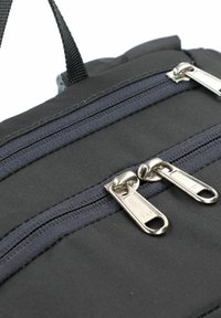 Detail van een zwarte stoffen rugzak met twee zilverkleurige ritsen en donkerblauwe accenten, een gestructureerd oppervlak en een stevige handgreep.