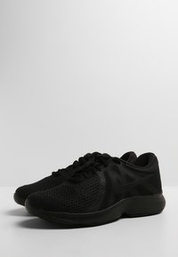 Par de zapatillas de running Nike negras con tela de malla y suelas acolchadas colocadas una al lado de la otra sobre una superficie blanca.