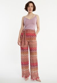 Camisole violet clair à fines bretelles accompagné d'un pantalon large avec un motif en zigzag dans des tons de rouge, d'orange et d'or.