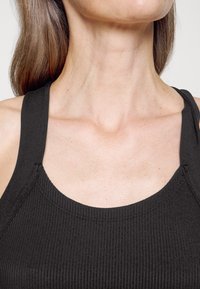 Camisola preta com nervuras, de alças largas, com decote em forma de scoop e textura suave, mostrando uma vista em close da parte superior do peito.
