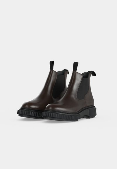 Bottes Chelsea en cuir brun foncé avec semelles épaisses noires rainurées et languettes, montrées sur un fond clair uni.