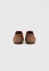 Brown suede low-top sneakers viewed from the back on a plain white background.