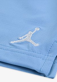 Ανοιχτό μπλε ύφασμα με ομαλή υφή που διαθέτει ένα εμφανές λευκό κεντημένο λογότυ πο Jumpman. Οι άκρες παρουσιάζουν καθαρά ραφικά στοιχεία.