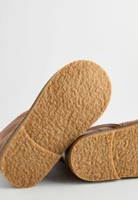 Bruine leren schoenzolen met een gestructureerde, rubberachtige afwerking; ronde vorm en licht opstaande randen, met een gladde beige rand.
