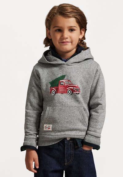 Haut à capuche gris avec un graphique d'un camion vintage rouge portant un sapin de Noël. Il a une poche avant et des poignets côtelés. Associé avec un jean foncé.