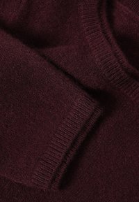 Bordo krāsa, viegla adīta džempera, kas izgatavots no mīksta materiāla ar ribotām piedurknēm un apakšmalu. Audums izskatās nedaudz pūkains un teksturēts.