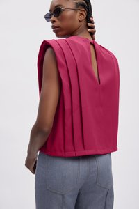 Haut sans manches fuchsia avec un design plissé et un dos en forme de clé, fabriqué en tissu lisse. Associé à un pantalon taille haute en denim gris.